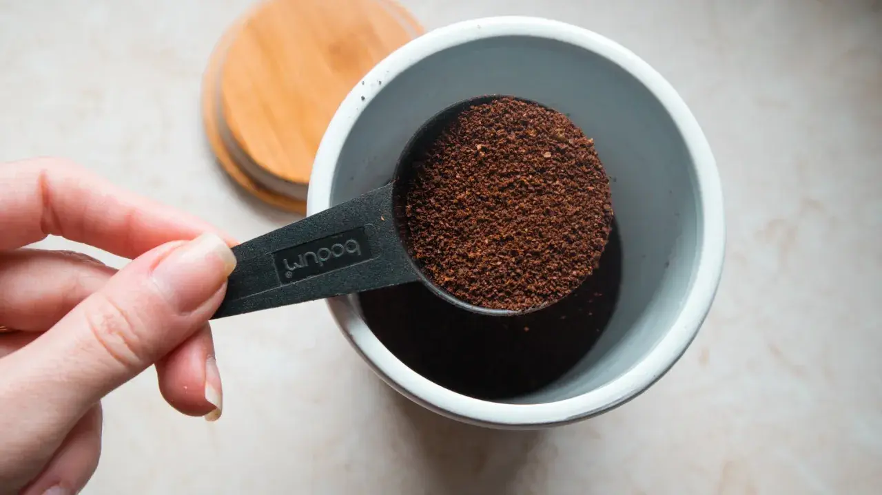 Eine Hand hält einen Löffel mit Kaffeepulver, bereit, ihn in einen Behälter zu geben. Die Frage ist: wieviel kaffeepulver auf 1 liter wasser?