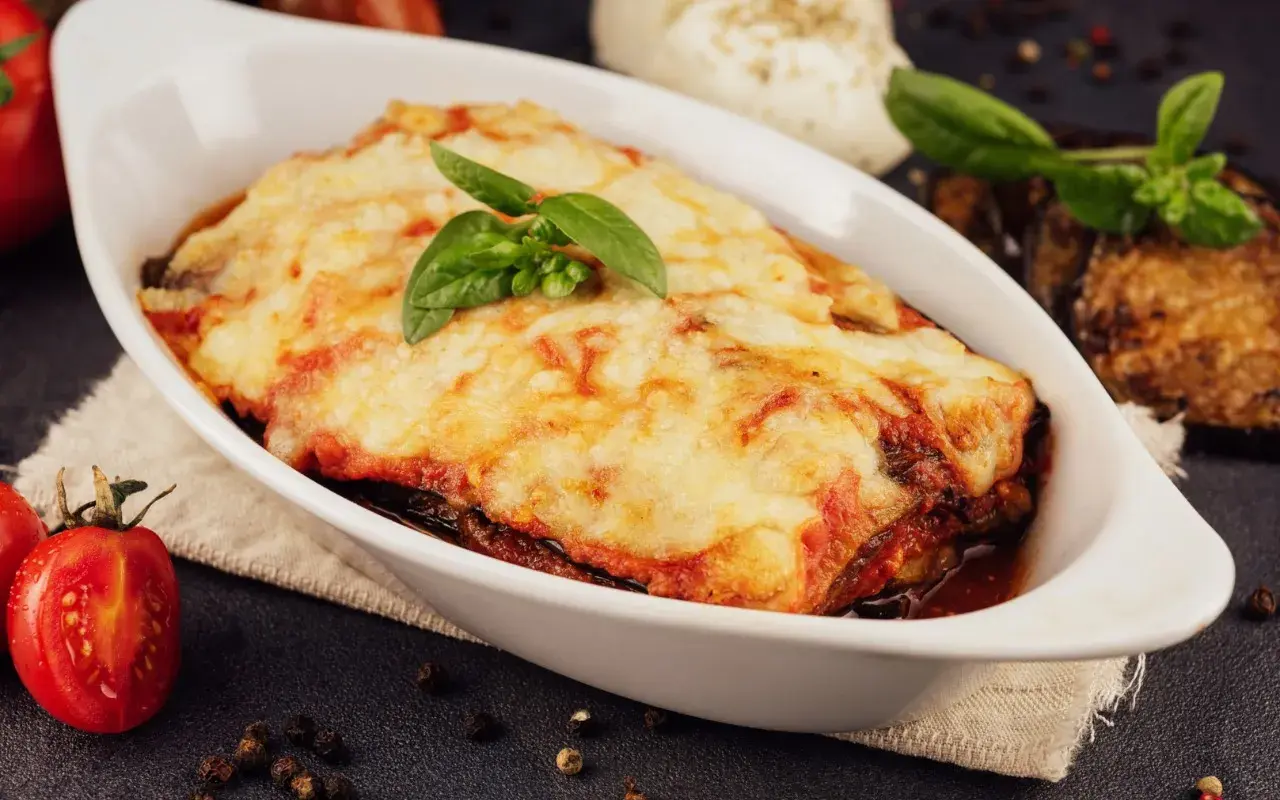 Herzhafte Auberginen Lasagne mit geschmolzenem Käse und frischem Basilikum, serviert in einer weißen Auflaufform.