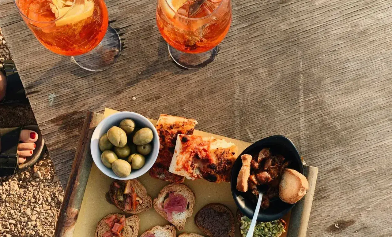 Zwei Aperol Spritz und eine Auswahl an italienischen Aperitif-Spezialitäten: Oliven, Bruschetta und Pizza.