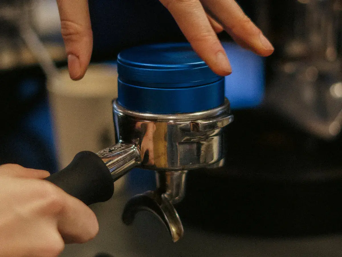 Barista bereitet Espresso zu, indem er den Tamper auf den Kaffeepuck im Siebträger drückt.