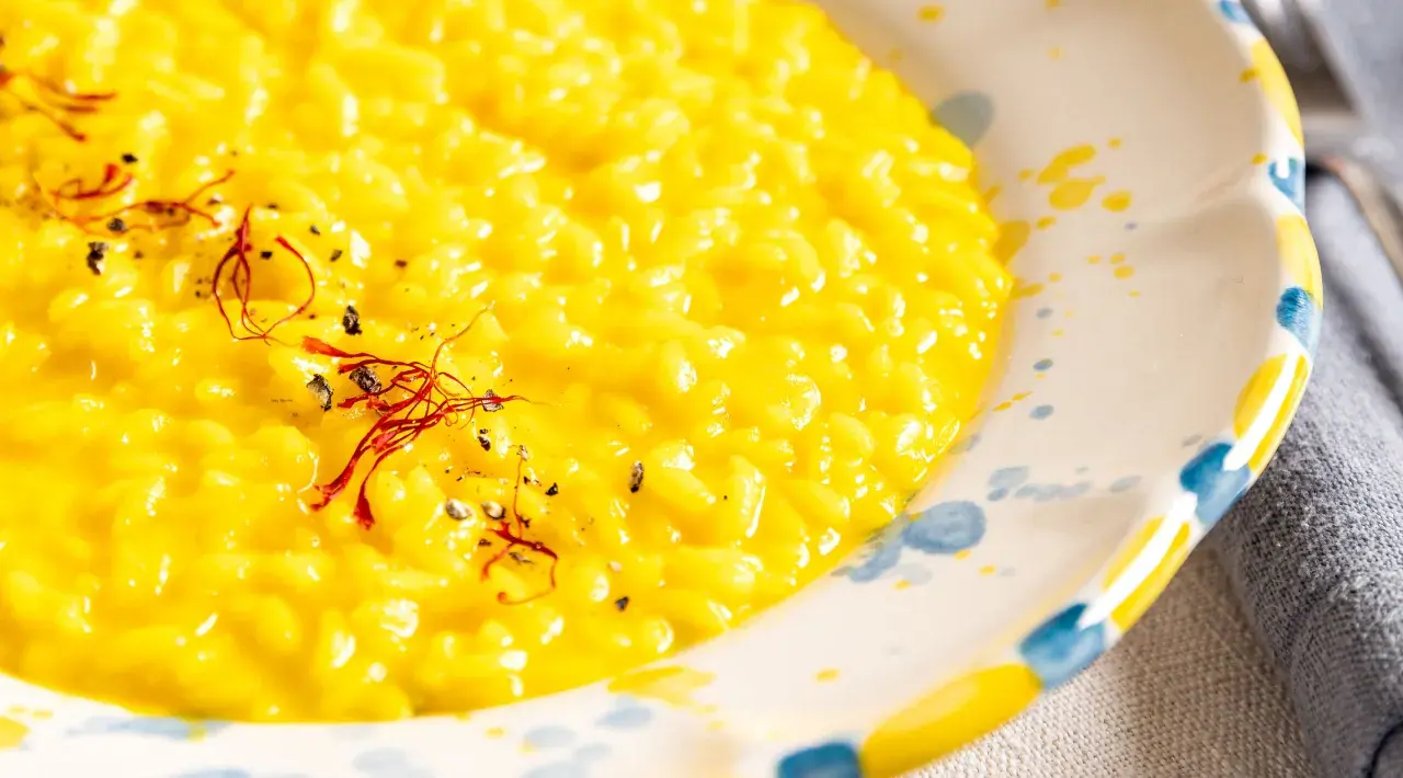 Cremiges, gelbes Risotto Milanese, garniert mit Safranfäden und schwarzem Pfeffer, in einem handbemalten Teller.
