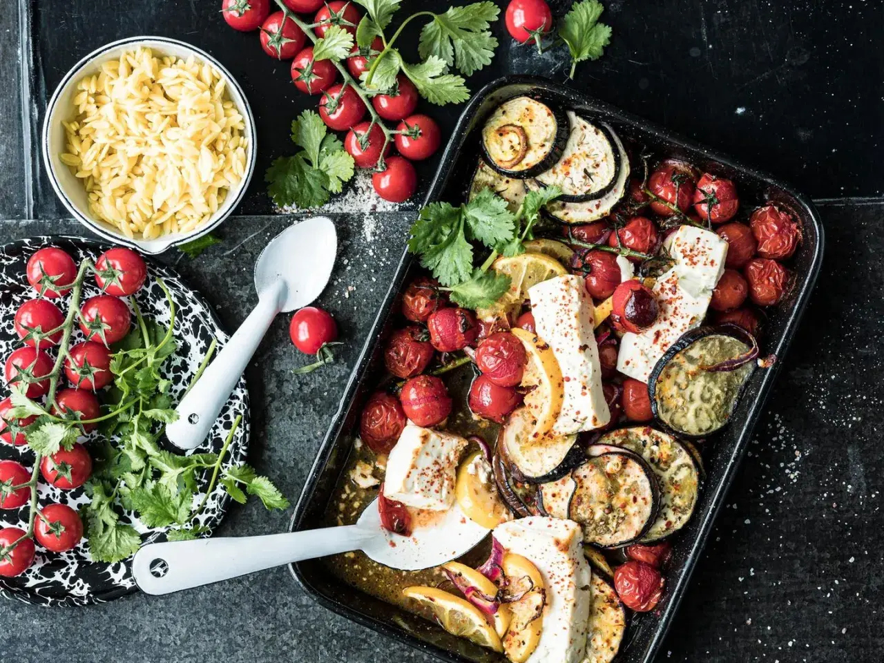 Ofenfrisches Gericht mit Aubergine, Tomaten und Feta. Dazu Orzo-Nudeln und frische Kräuter.