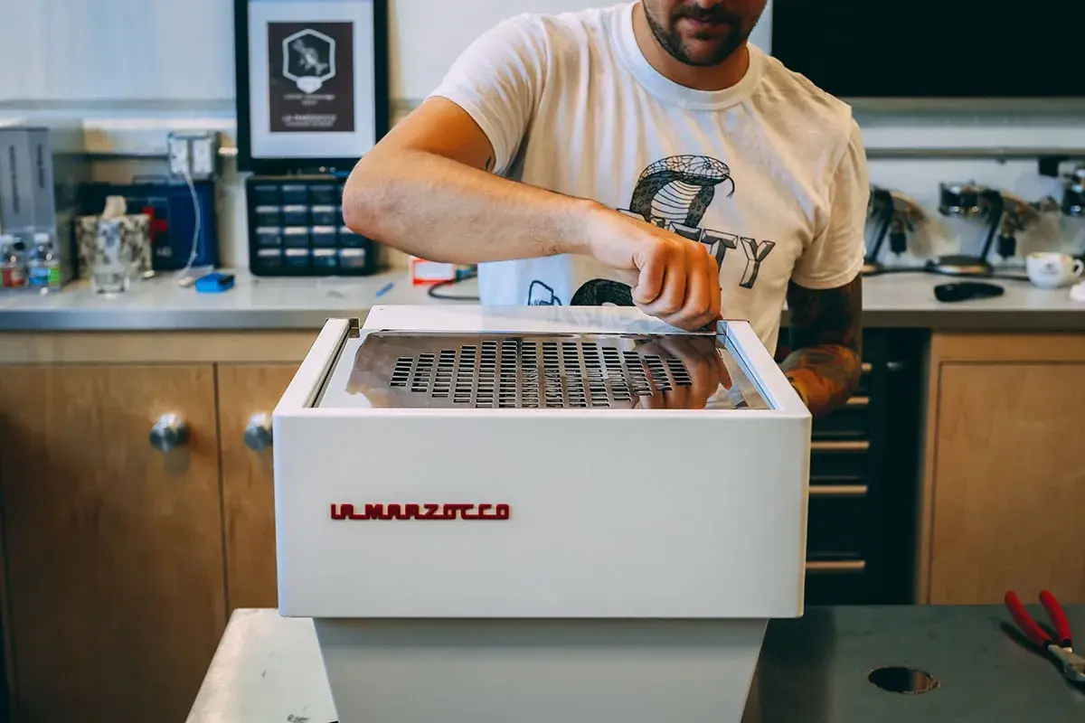Mann reinigt eine La Marzocco Espressomaschine. Sorgfältige Pflege für perfekten Kaffeegenuss.