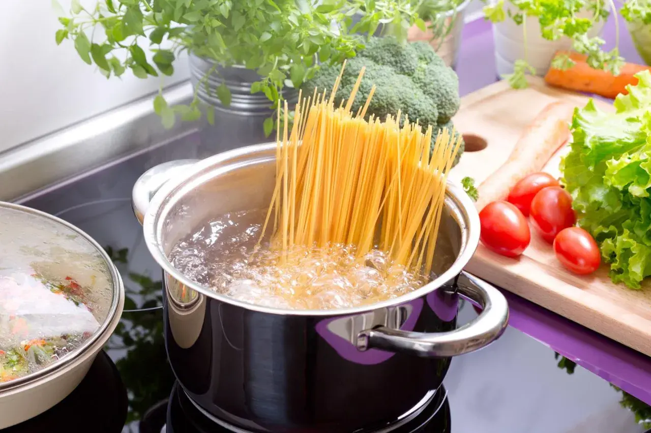 Spaghetti kochen in sprudelndem Wasser. Die genaue Zeit, wie lange nudeln kochen, hängt von der Sorte ab. Frische Kräuter und Gemüse liegen bereit.