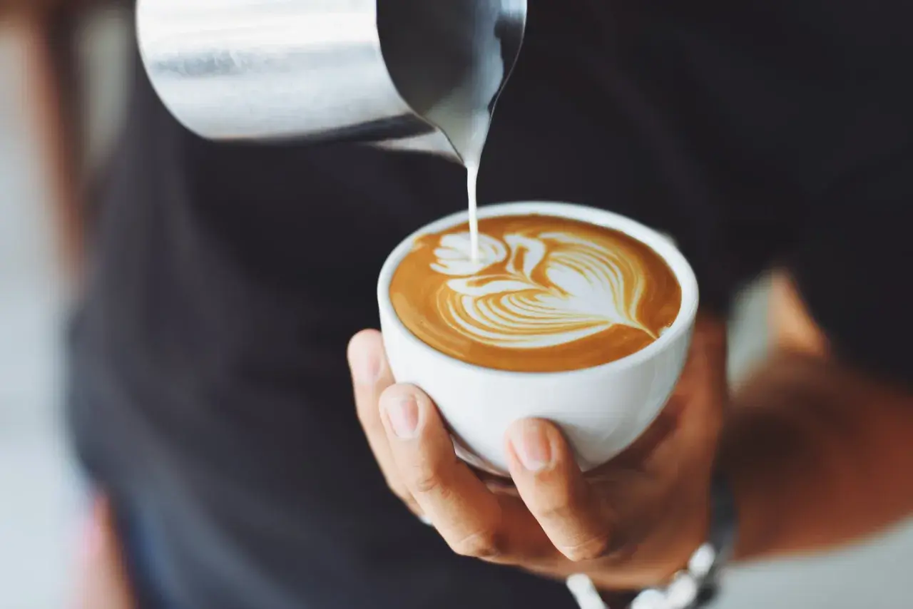 Ein Barista gießt Milch in eine Tasse, um ein Latte Art Muster zu kreieren. Ein perfekter Kaffee auf italienisch.