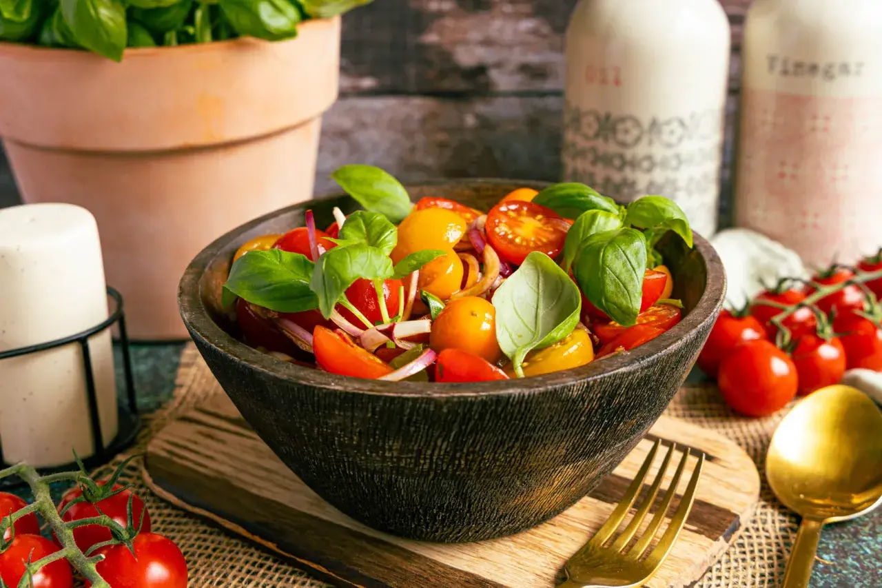 Frischer Tomatensalat italienisch mit Basilikum, Zwiebeln und Kirschtomaten in einer Holzschale.