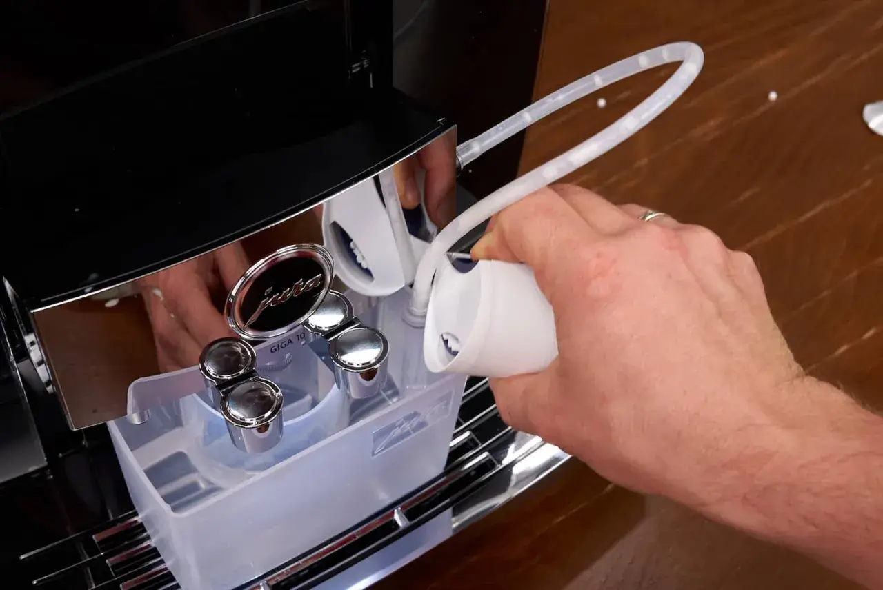 Hand füllt Entkalkungsmittel in eine Jura Kaffeemaschine. Regelmäßiges Entkalken sorgt für Langlebigkeit.