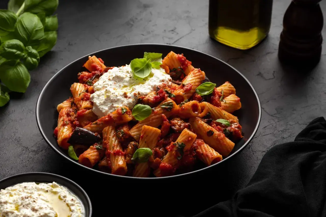 Rigatoni mit Auberginen-Tomaten-Sauce und cremigem Ricotta – ein Beweis für die besten Rezepte mit Auberginen. Frischer Basilikum und Olivenöl runden das Gericht ab.