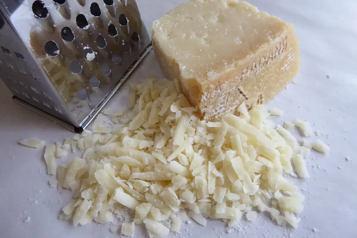 Ein Stück Pecorino liegt neben frisch geriebenem Käse und einer Reibe. Der Kampf Pecorino vs Parmesan beginnt!