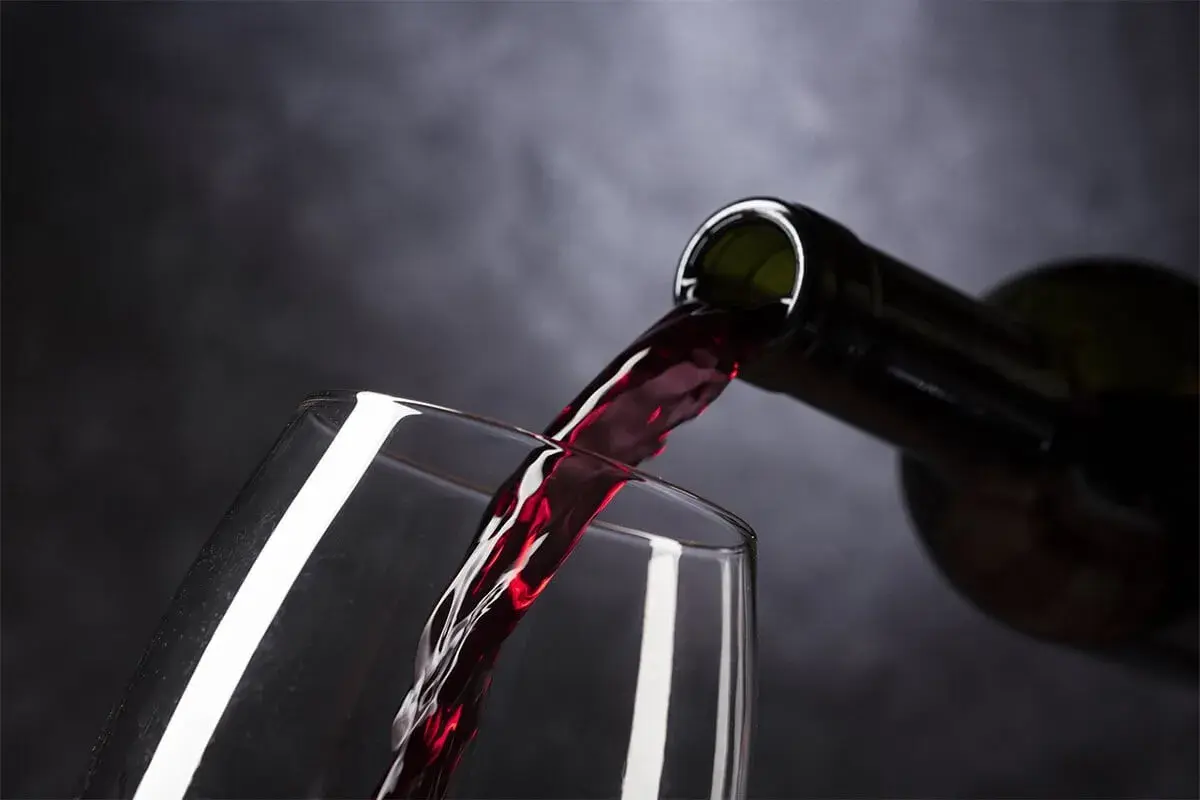 Rotwein fließt aus einer Flasche in ein Glas. Ist Wein vegan? Ja, dieser Wein ist vegan.