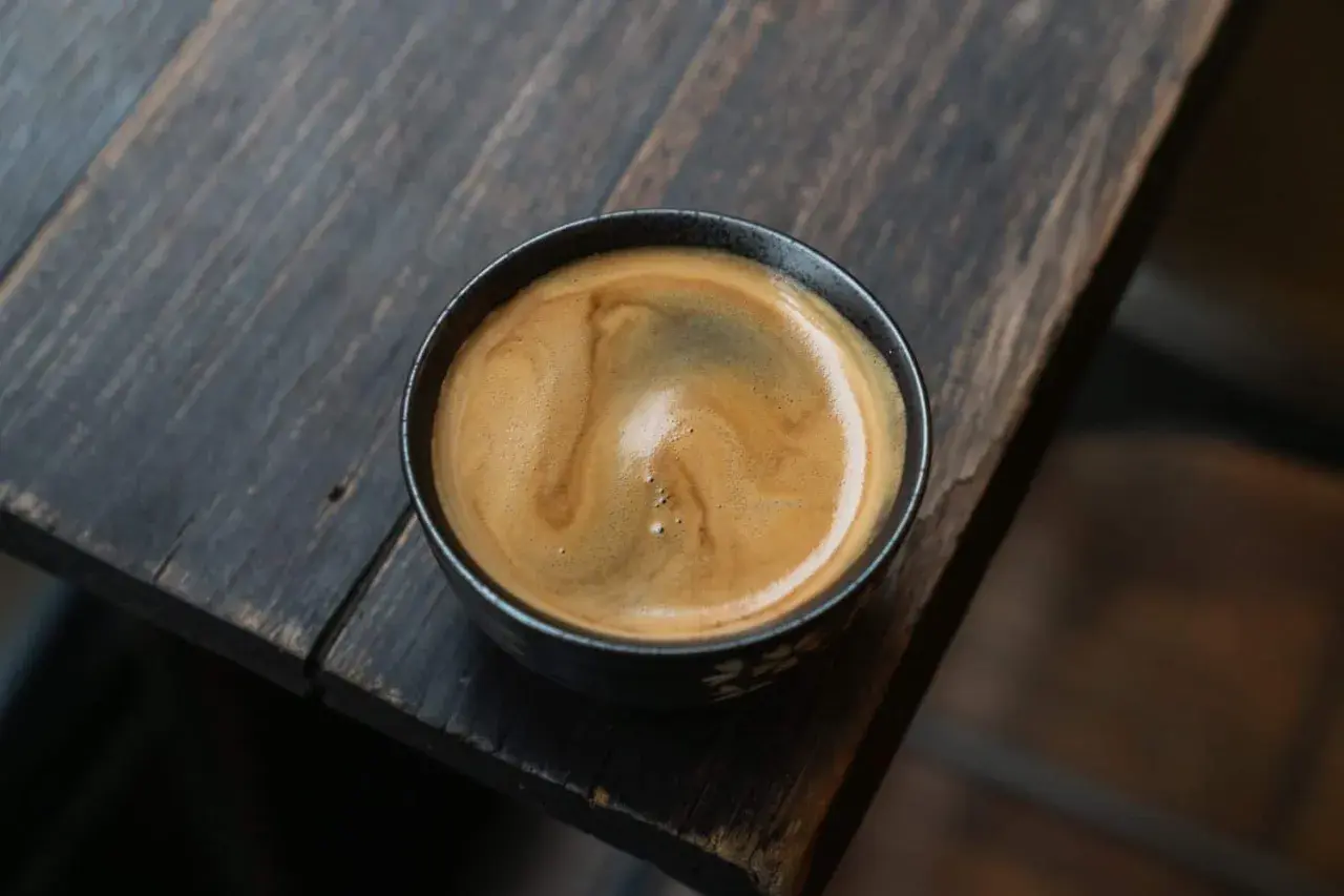 Ein dampfender americano kaffee mit schöner Crema in einer dunklen Tasse auf einem rustikalen Holztisch.