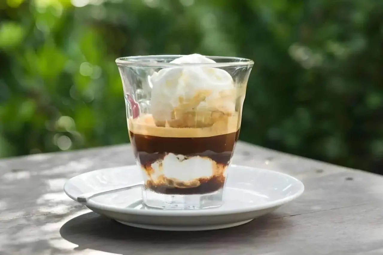 Ein Glas mit Espresso und Vanilleeis, das auf einem Tisch im Freien steht.