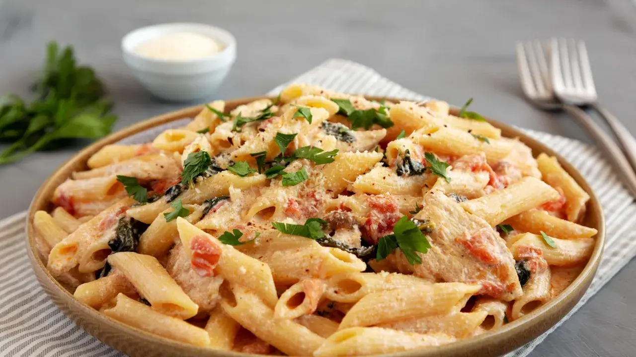 Cremige Penne mit sonnengetrockneten Tomaten, Spinat und Parmesan, garniert mit frischer Petersilie. Ein köstliches Gericht, das Lust auf mehr macht.