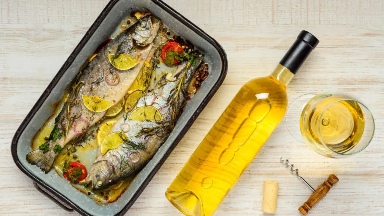Zwei gebackene Forellen mit Zitrone und Kräutern, daneben eine Flasche Weißwein und ein Glas. Perfekt, welcher Wein zu Fisch passt!