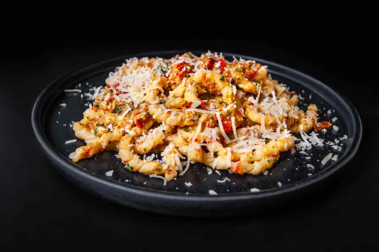 Gedrehte Pasta mit Pesto Trapanese, Tomaten und geriebenem Käse auf einem dunklen Teller.