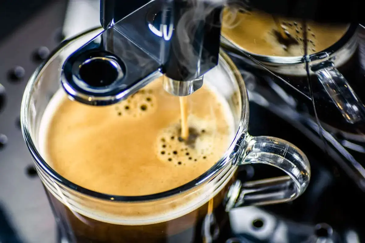 Frisch gebrühter Espresso fließt aus einem Vollautomaten in eine Glas Tasse. Der Kaffee schmeckt bitter, aber die Crema ist perfekt.