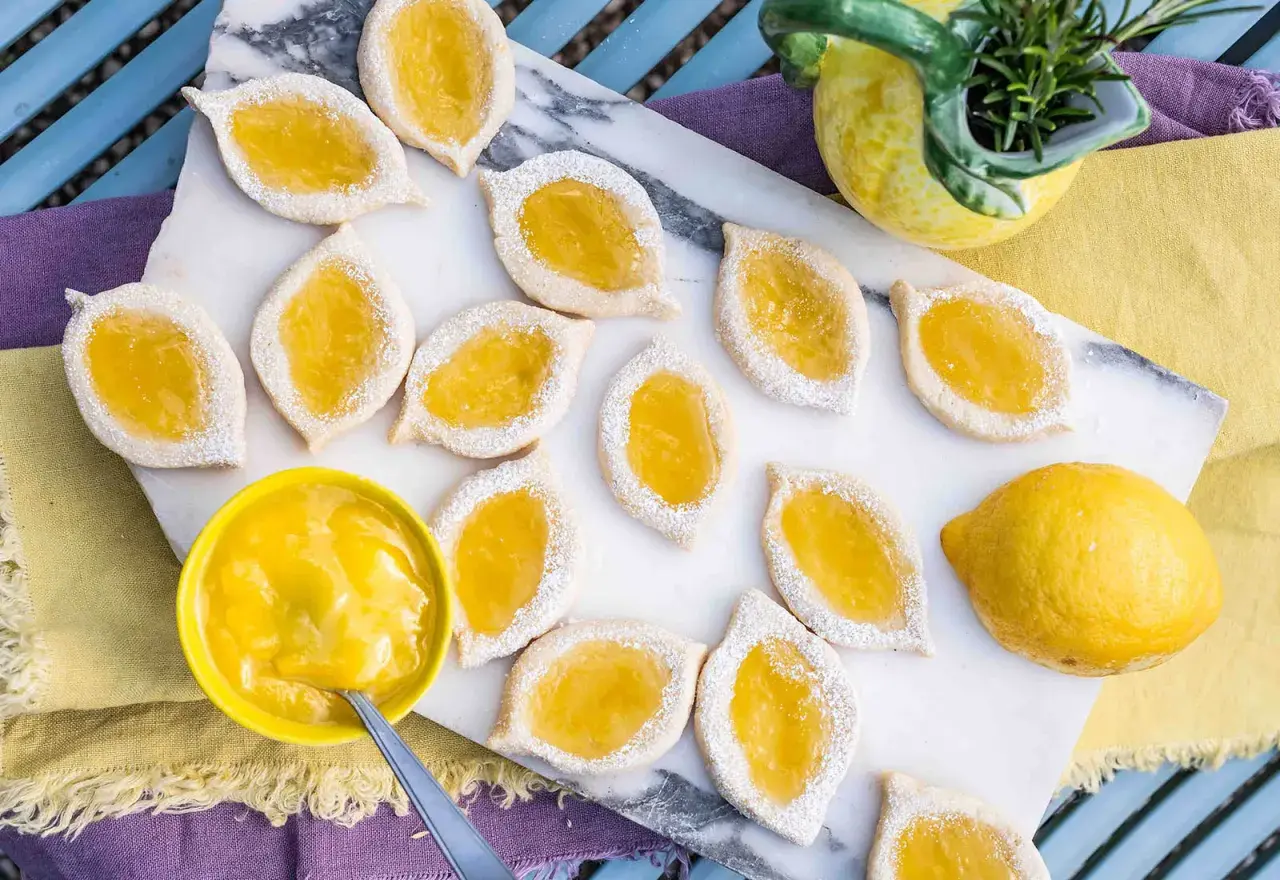 Zitronenkekse italienisch, mit leuchtend gelber Zitronencreme gefüllt und mit Puderzucker bestäubt, liegen auf einem Marmorbrett.