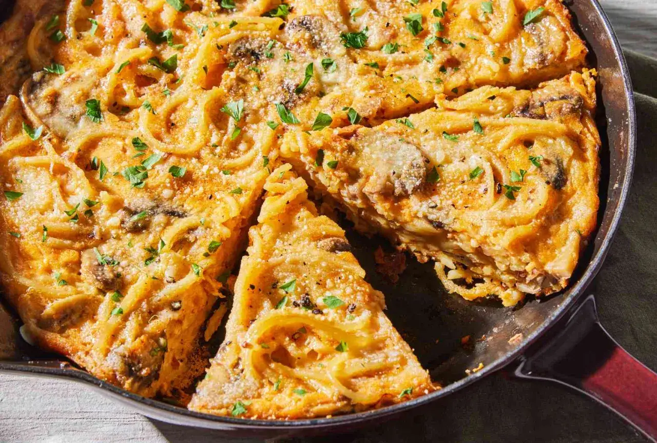 Eine goldbraune Frittata di Pasta mit Spaghetti, Pilzen und Käse, garniert mit Petersilie.