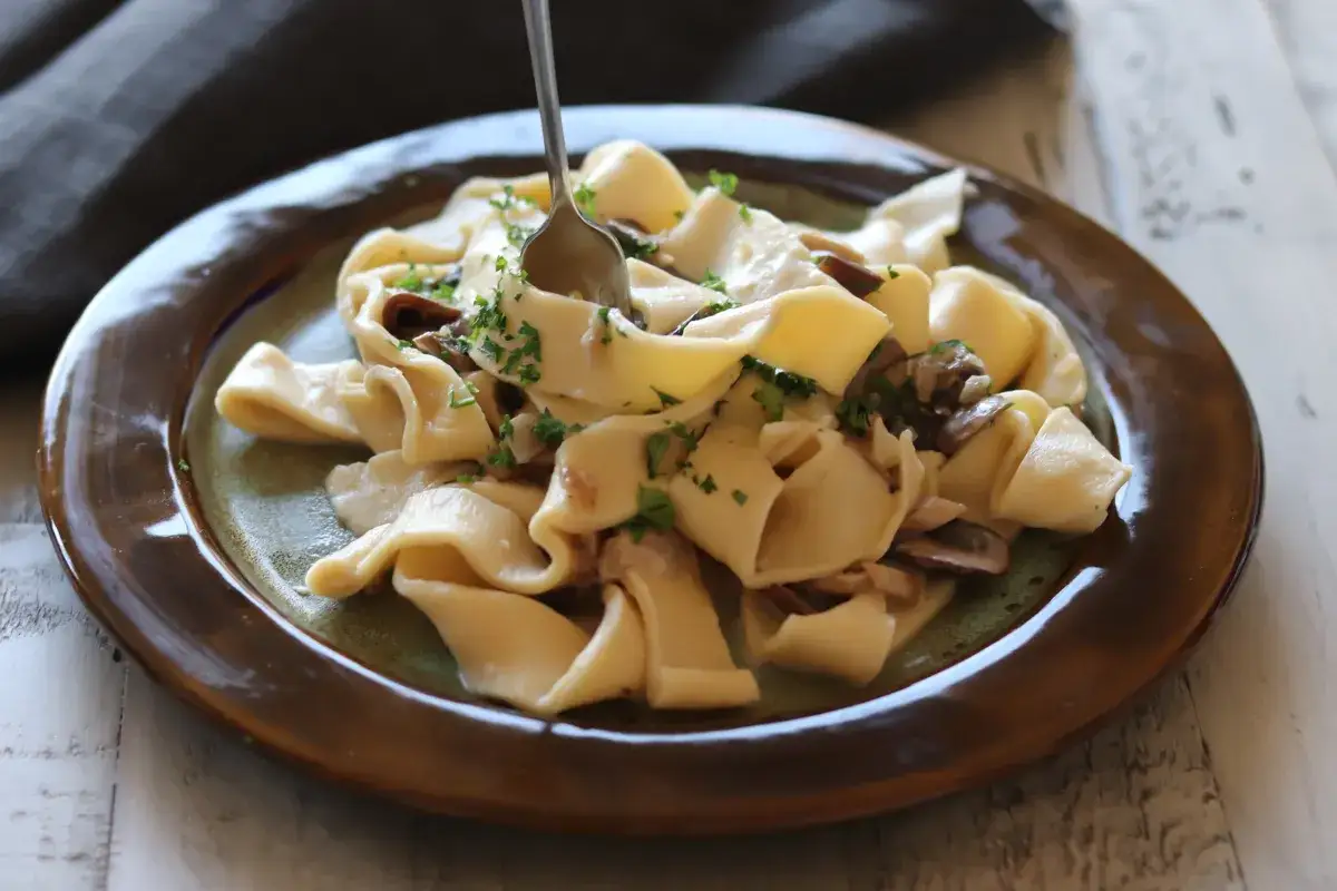 Breite Bandnudeln mit cremiger Pilzsauce und Petersilie, ein köstliches italienisches Gericht.