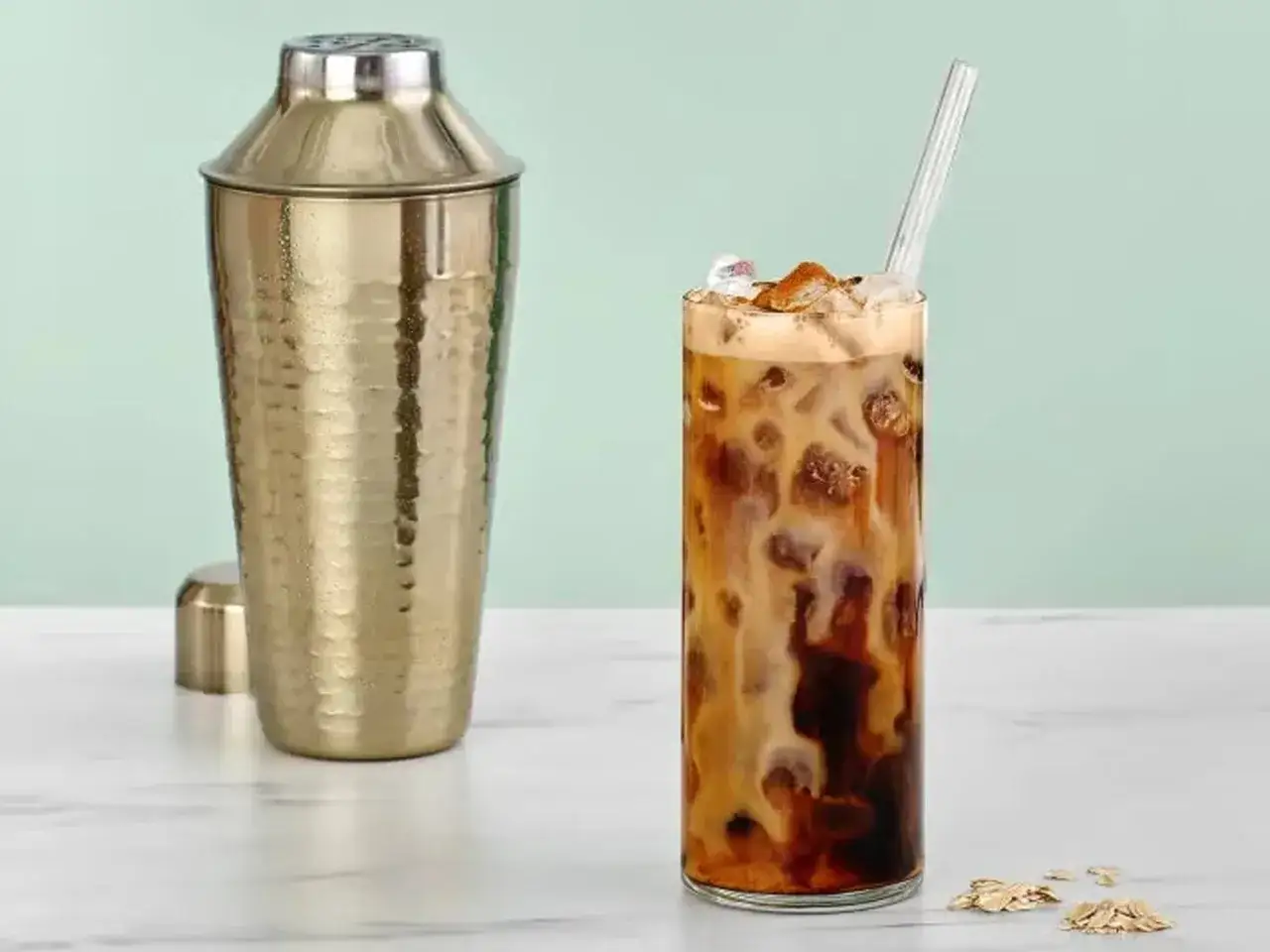 Ein erfrischender Espresso Freddo mit Eis und Milch, daneben ein goldener Cocktail-Shaker.