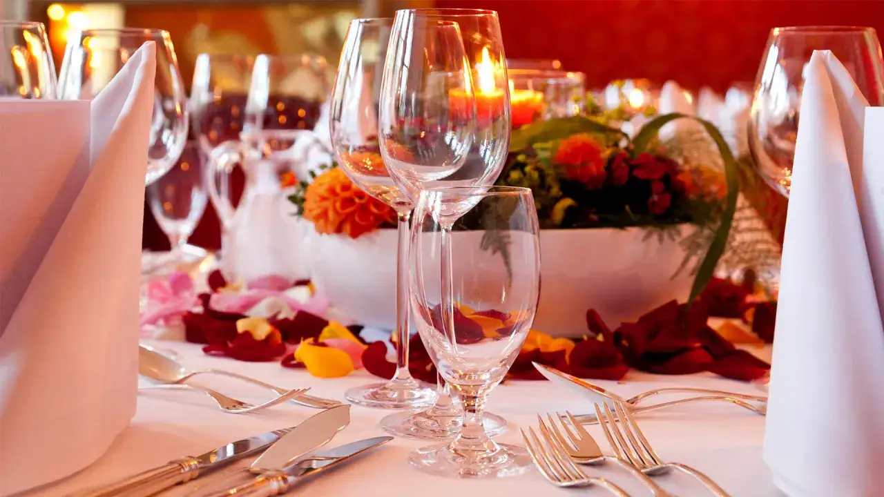 Festlich gedeckter Tisch mit Rosenblättern, Kerzenlicht und Gläsern, bereit für ein romantisches Essen mit Wein zum Essen.