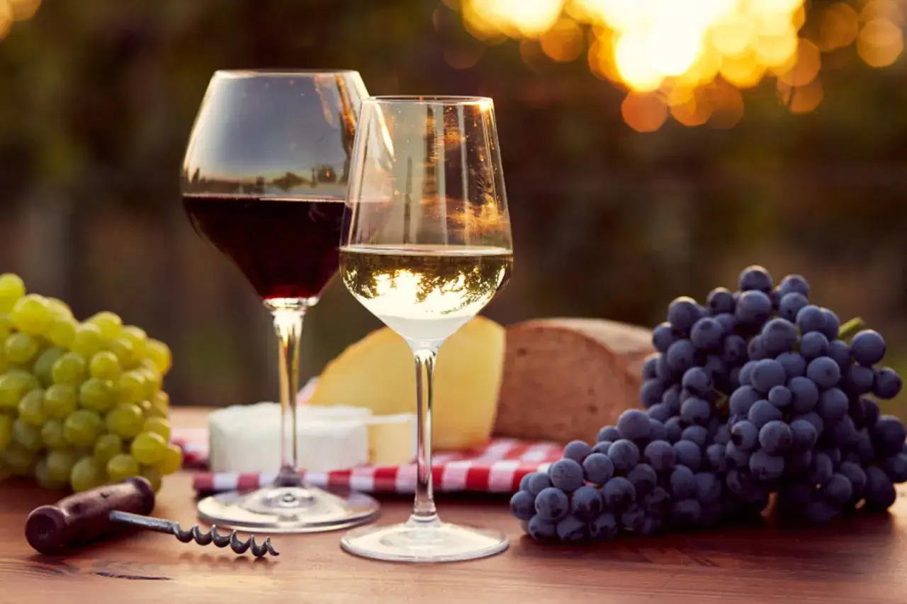 Zwei Gläser Wein, Trauben, Käse und Brot auf einem Holztisch. Der Rotwein hat einen Zuckergehalt von ca. 0,5g pro 100ml.