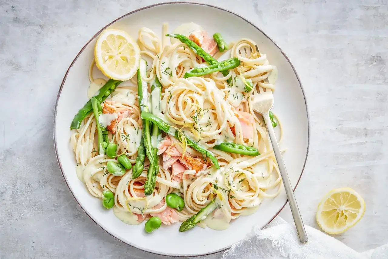 Lachs mit Tagliatelle, Spargel und Erbsen in cremiger Sauce, garniert mit Zitrone und Dill. Ein k&ouml;stliches Gericht!