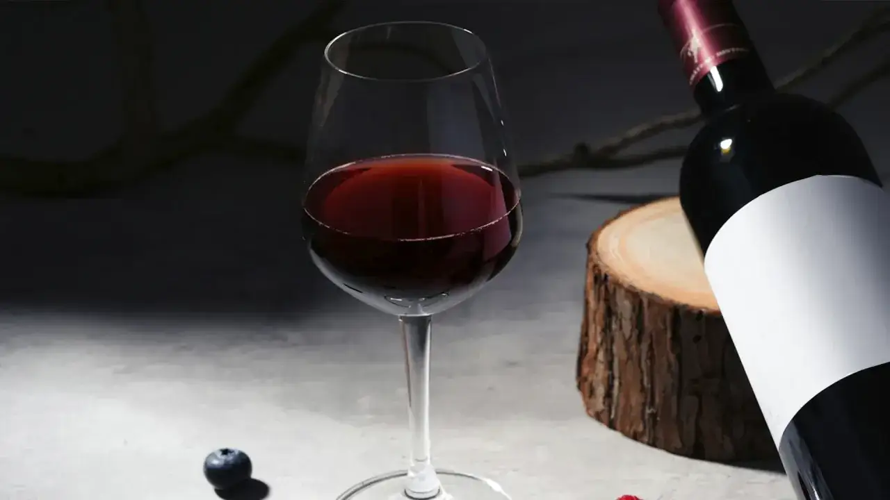 Ein Glas Rotwein, perfekt temperiert für den Genuss von Primitivo, neben einer Flasche und Beeren.