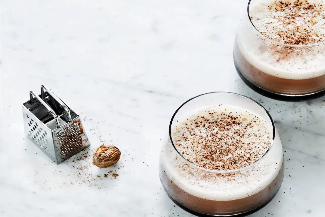 Zwei Gl&auml;ser mit cremigem Kaffee-Cocktail, bestreut mit frisch geriebener Muskatnuss. Daneben liegen eine Muskatnuss und ein kleines Reibeisen.
