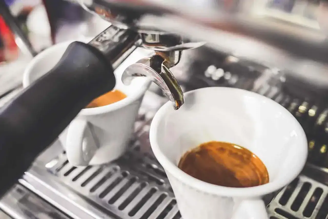 Frisch gebrühter Kaffee auf Italienisch fließt in zwei weiße Tassen aus einer Espressomaschine.