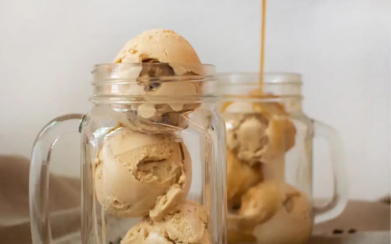 Eiscreme mit karamellfarbenem Topping in Gläsern. Ein Schwall Soße fließt über das Eis, ein perfekter kalter Kaffee-Genuss.