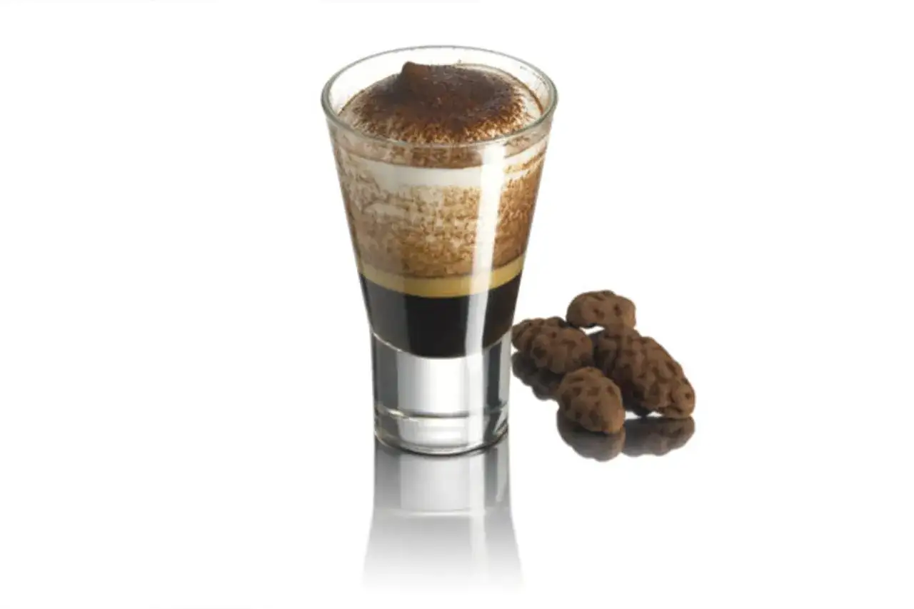 Ein Caffe Marocchino mit cremigem Schaum und Kakaopulver, daneben ein paar schokoladige Kekse.