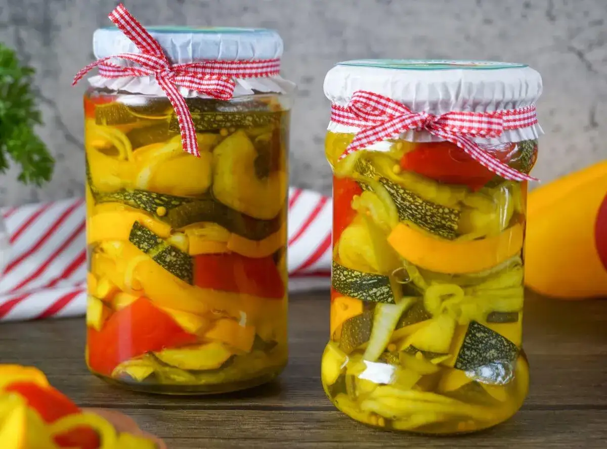 Zwei Gl&auml;ser mit eingelegtem Gem&uuml;se, bereit zum Einkochen. Bunte Zucchini- und Paprikastreifen in Essigsud, mit rot-wei&szlig; kariertem Band verziert.