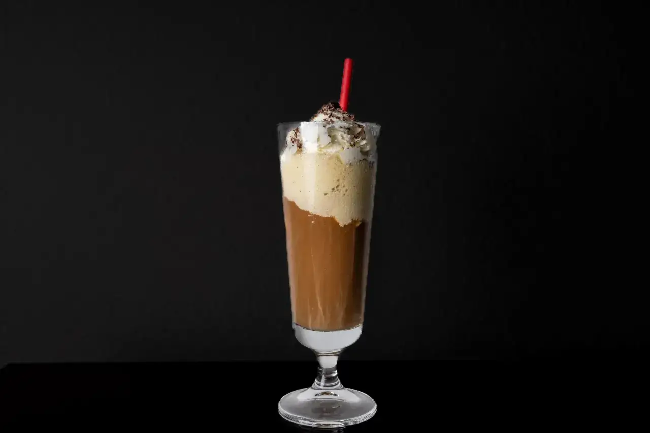 Ein cremiger Eiskaffee ohne Eis, gekr&ouml;nt mit Sahne und Schokostreuseln, serviert mit einem roten Strohhalm.