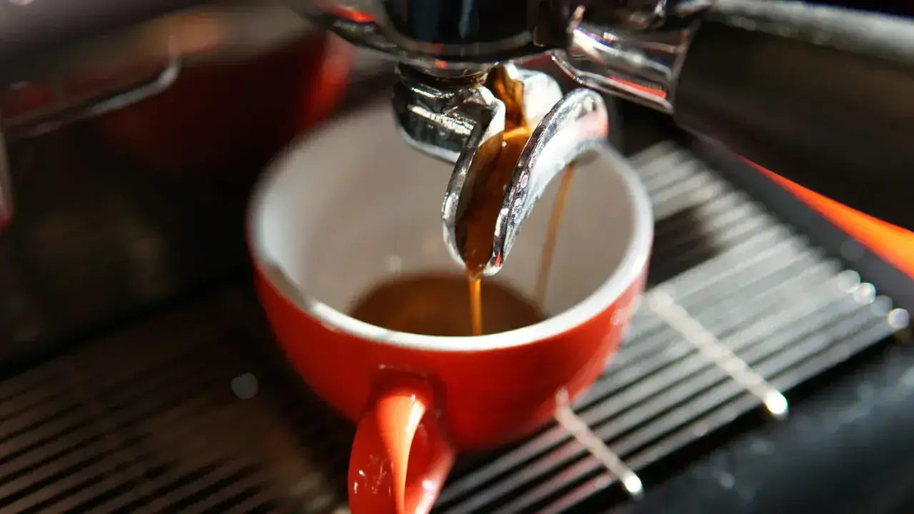 Frisch gebrühter Espresso läuft in eine rote Tasse. Hoffentlich ist er nicht zu bitter.