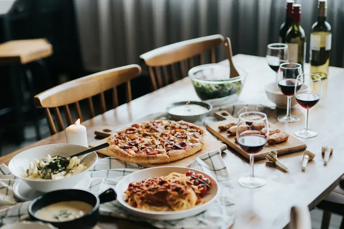 Gemütliches Abendessen mit Pizza, Pasta, Salat und Rotwein. Kerzenlicht und ein gedeckter Tisch laden zum Genießen ein.