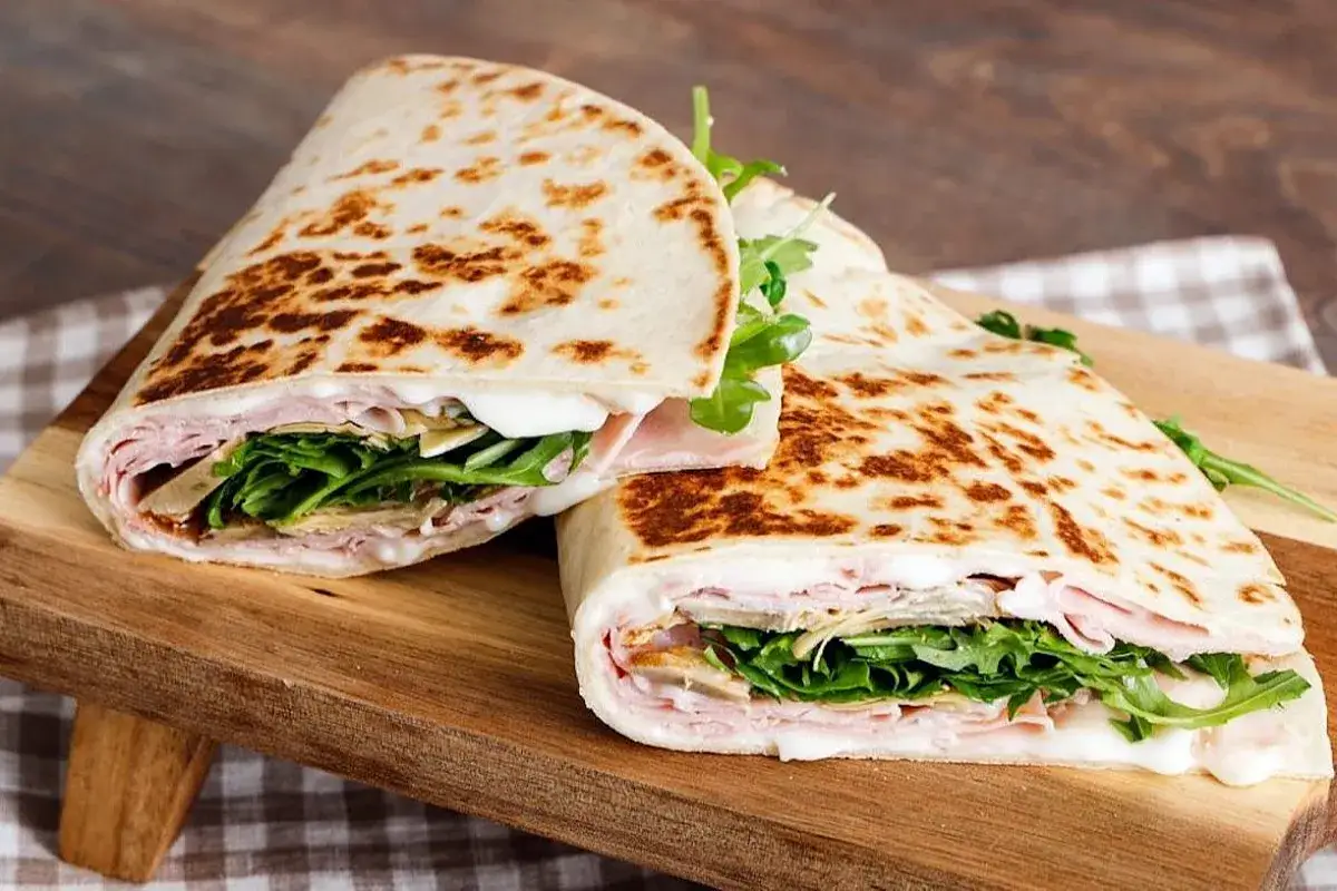 Zwei gef&uuml;llte Piadinas mit Schinken, Rucola und K&auml;se auf einem Holzbrett. Ein k&ouml;stliches Piadina Rezept.