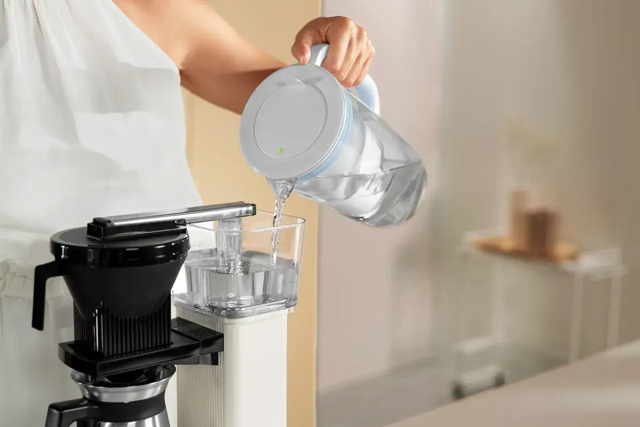 Frau f&uuml;llt Wasser in eine Kaffeemaschine. Regelm&auml;&szlig;iges Entkalken sorgt f&uuml;r perfekten Kaffeegenuss.