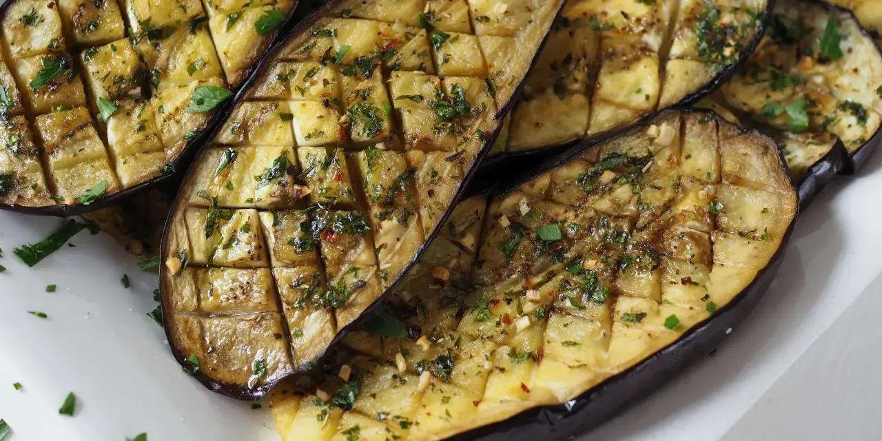 Ganze Aubergine im Ofen, karamellisiert und mit Kräutern und Knoblauch verfeinert. Ein köstliches Gericht, das auf einem Teller serviert wird.