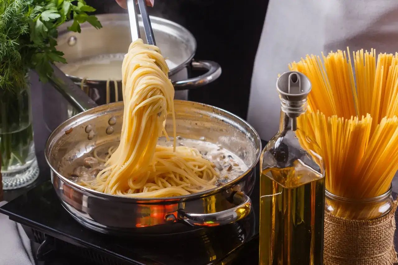 Frisch gekochte Spaghetti werden aus einem Topf in eine Pfanne mit cremiger Pilzsauce gehoben. Daneben stehen rohe Spaghetti und Olivenöl. Die Frage