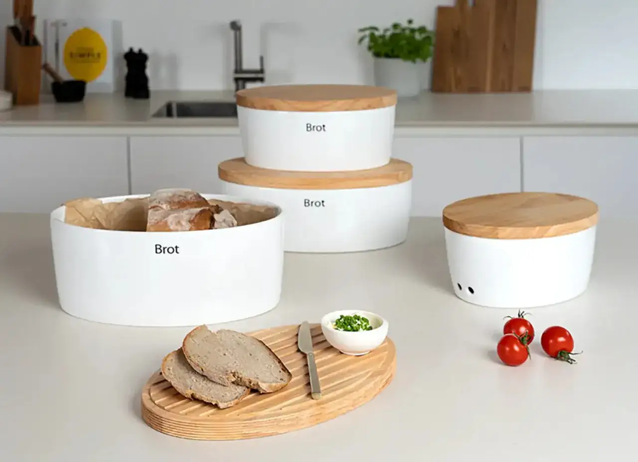 Moderne wei&szlig;e Brotdosen mit Holzdeckeln, ideal zum Brot aufbewahren. Eine Dose ist gef&uuml;llt, daneben liegen Brotscheiben.