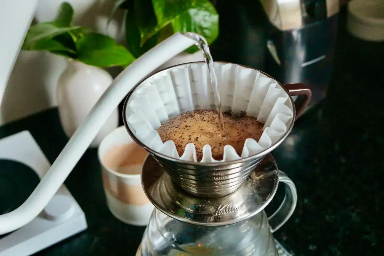 Heißes Wasser fließt über Kaffeepulver in einem Filter, um frischen Kaffee zuzubereiten. Der Pour-over-Prozess beginnt.