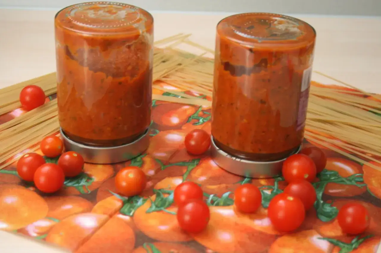 Zwei Gl&auml;ser mit selbstgemachter Tomatensauce, bereit zum Einkochen. Frische Kirschtomaten und Spaghetti liegen daneben.