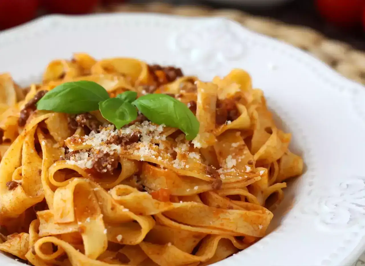 Ein Teller Tagliatelle mit einer herzhaften Bolognese-Sauce, garniert mit Basilikum und Parmesan. Ein Genuss wie beim spaghetti bolognese rezept original.