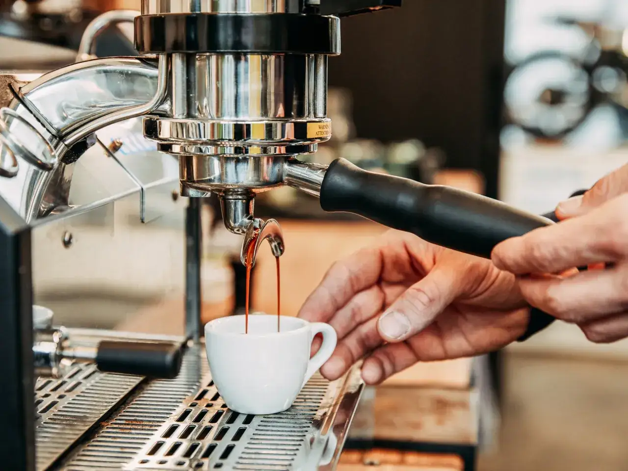 Barista bereitet Espresso zu. Hei&szlig;es, dunkles Gebr&auml;u flie&szlig;t aus der Maschine in eine kleine wei&szlig;e Tasse.