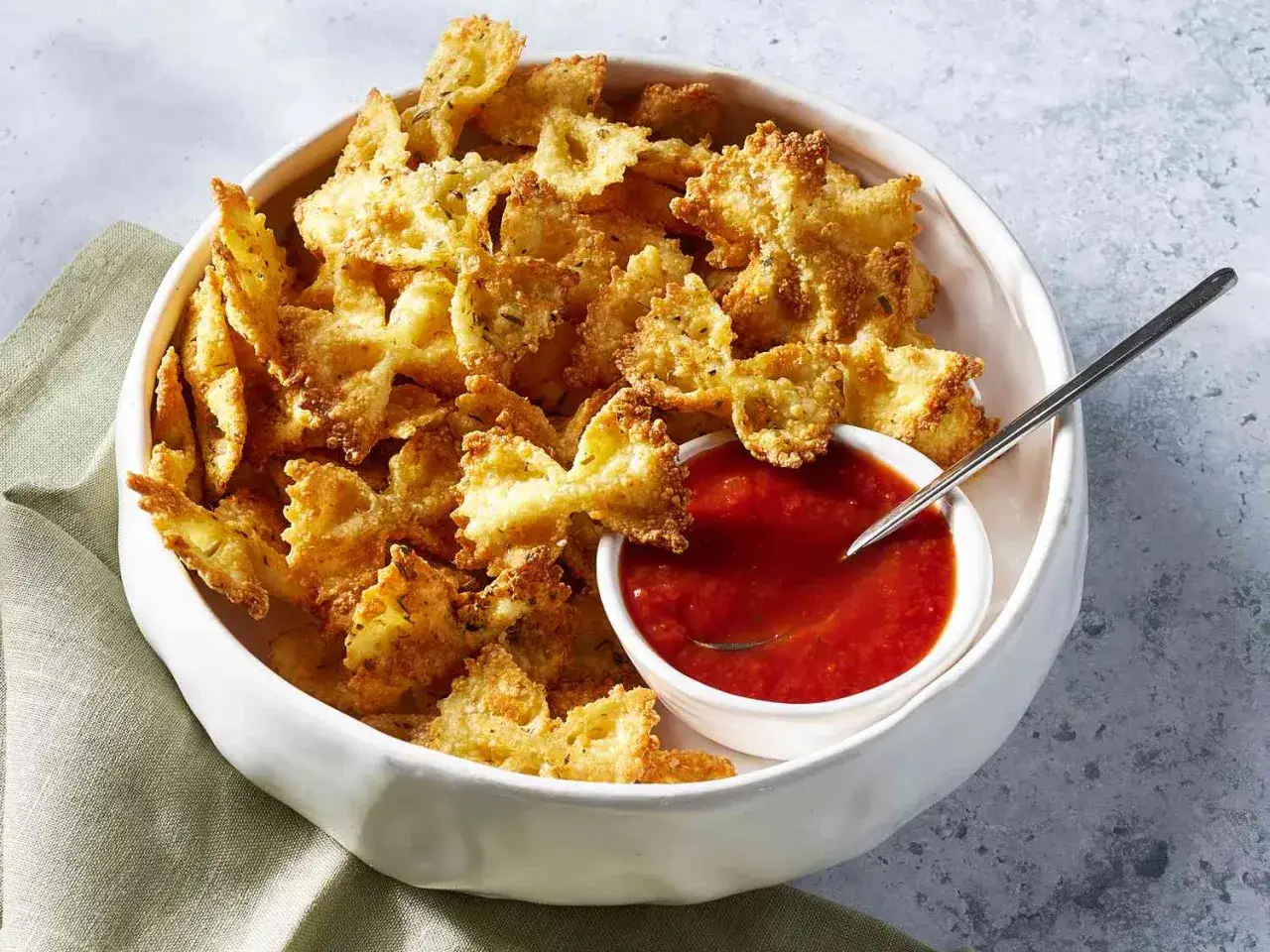 Knusprige Pasta Chips in Form von Schleifen, serviert mit einer Schale Tomatensauce. Ein leckerer Snack!