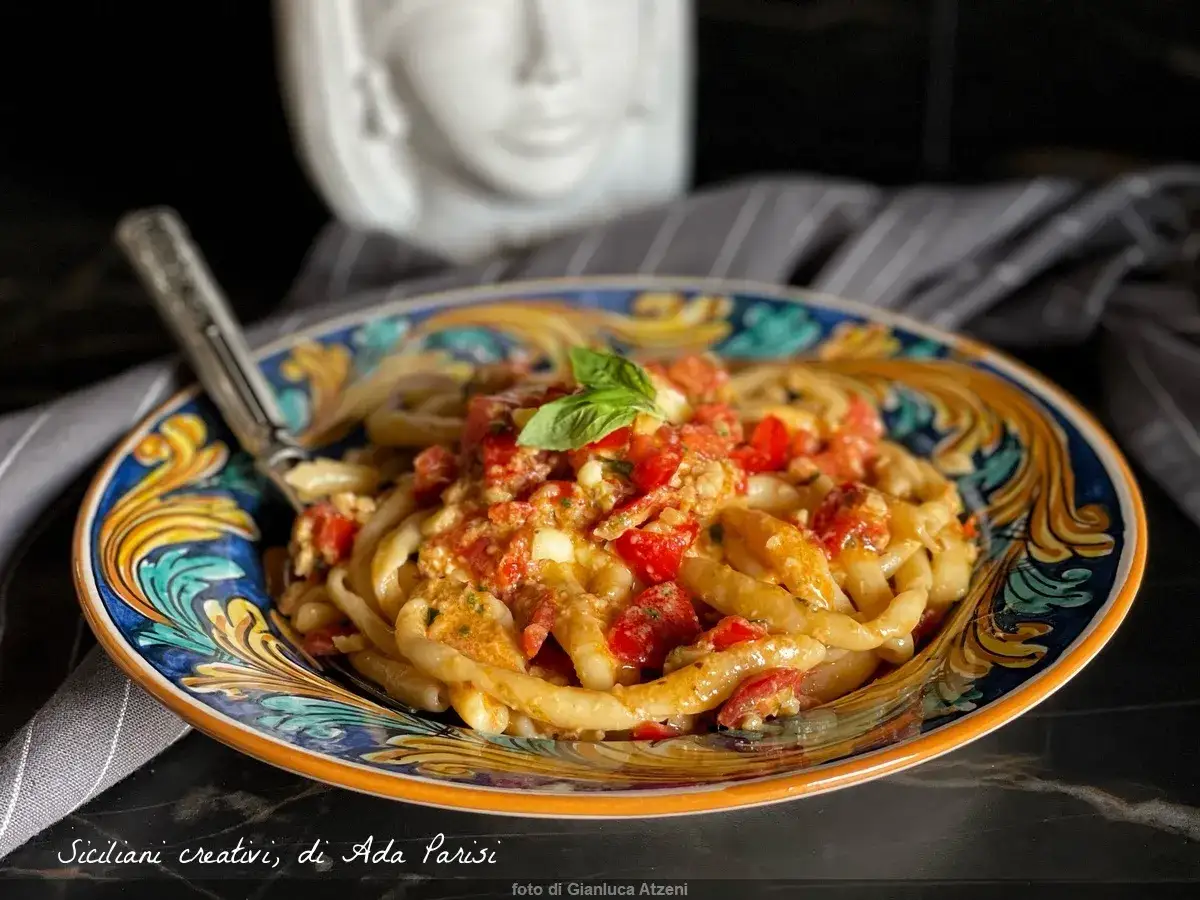 Hausgemachte Pasta mit Pesto Trapanese, Tomaten und Basilikum auf einem bunten Teller.
