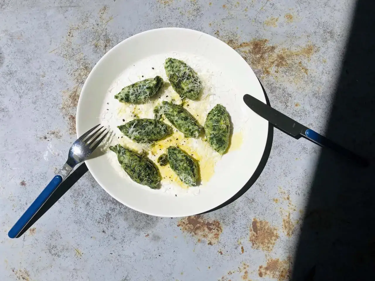 Grüne Malfatti, mit Parmesan bestreut, auf einem Teller mit Gabel und Messer. Ein leckeres Malfatti-Rezept zum Nachkochen.